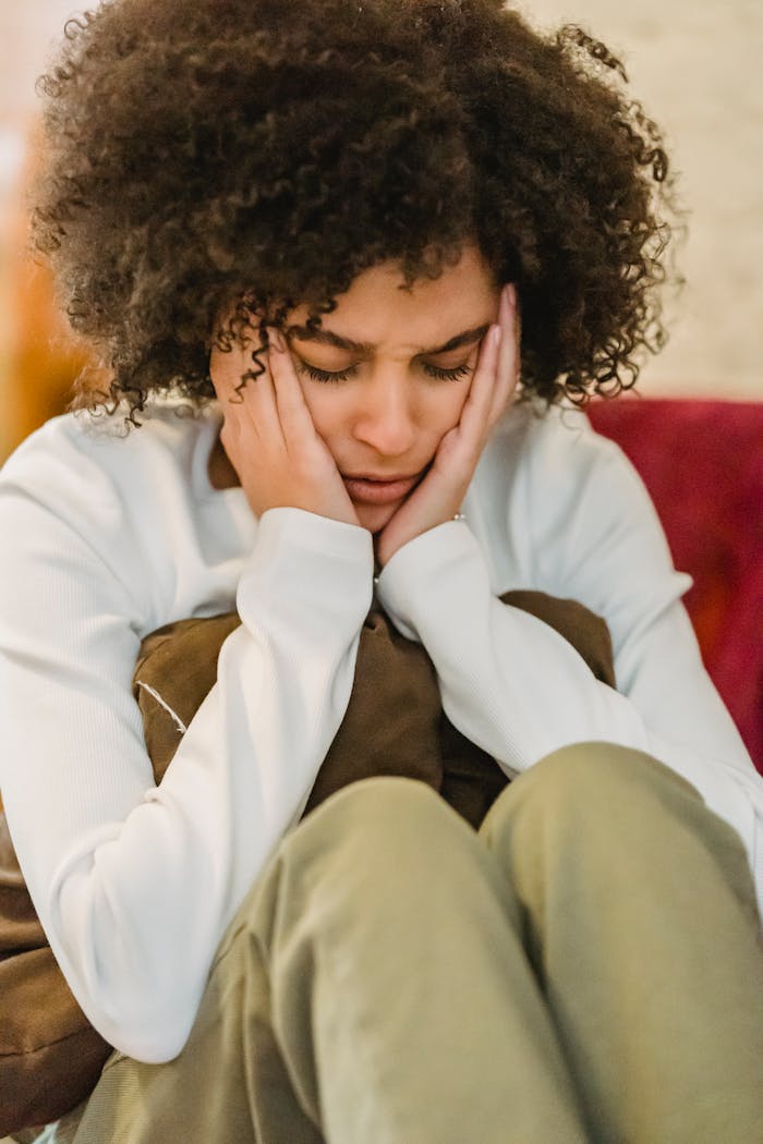 How Technology is Revolutionizing Pain Management Young sad ethnic lady in casual outfit sitting with pillow with hands on head and closed eyes in light room