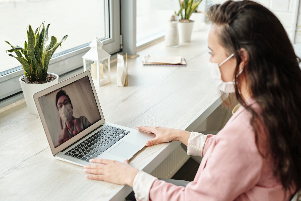 The Art of Drawing Readers In: Your attractive post title goes here Woman and doctor video calling on laptop, both wearing masks, symbolizing telehealth during COVID-19.