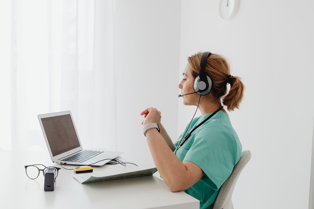 Mastering the First Impression: Your intriguing post title goes here A female doctor using a laptop for an online consultation, wearing a headset in a bright office.