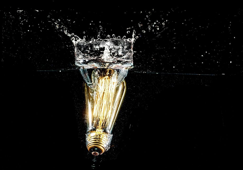 Lit bulb submerged in water, creating dramatic splash effect on black background.